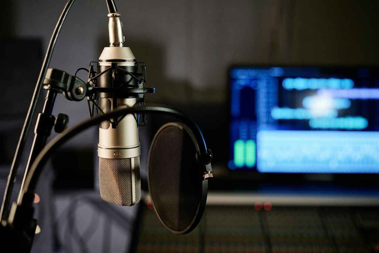 Microphone professionnel de studio avec filtre anti-pop devant un écran d'enregistrement audio - Studio d'annonces Saylo